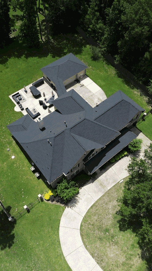 Aerial view of dark completed shingle roof surrounded by mature trees