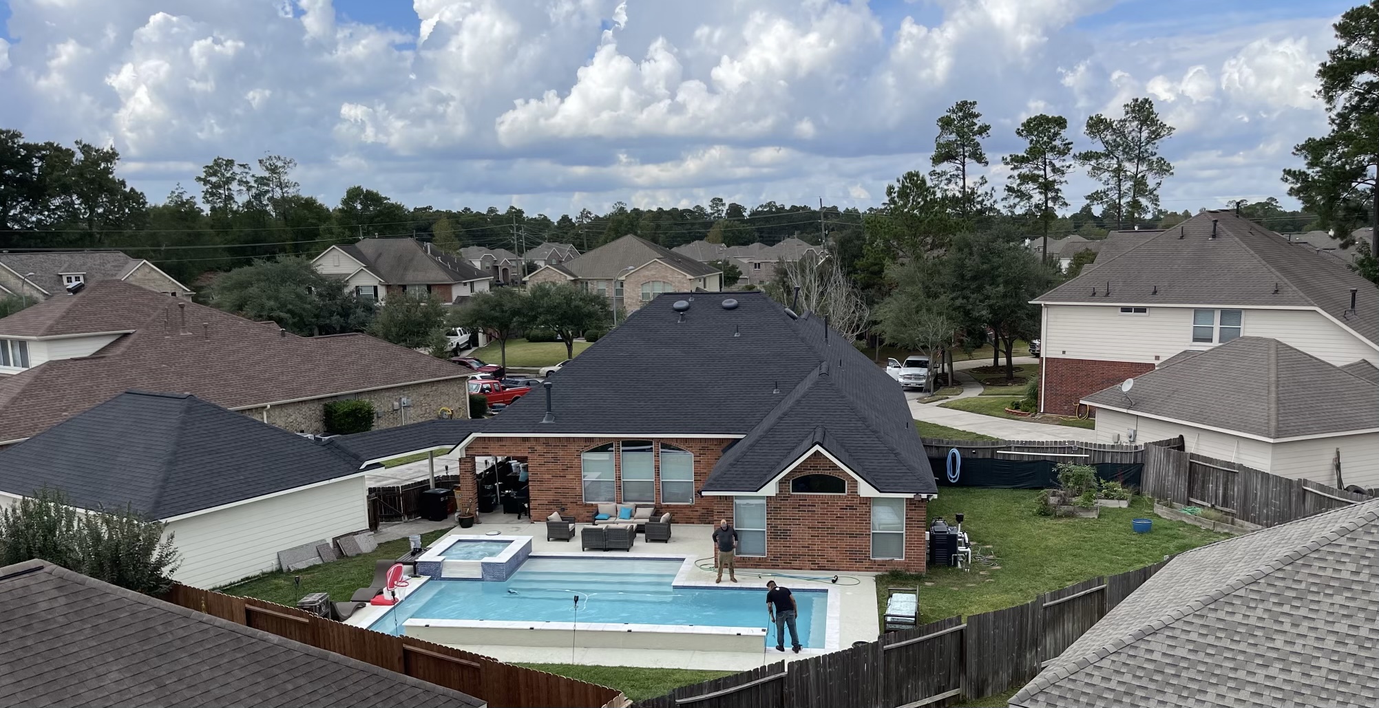 Aerial elevated view of completed black shingle roof on residential home with pool