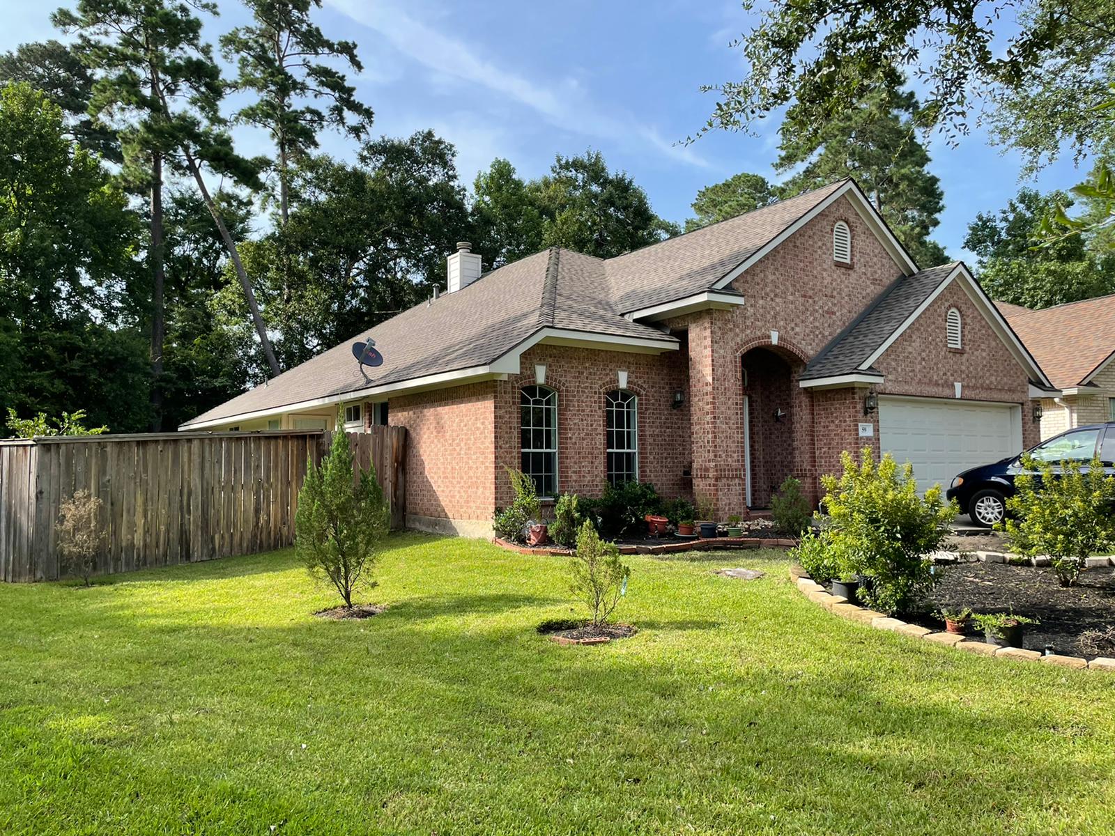 Completed grey shingle roof on brick home with mature landscaping