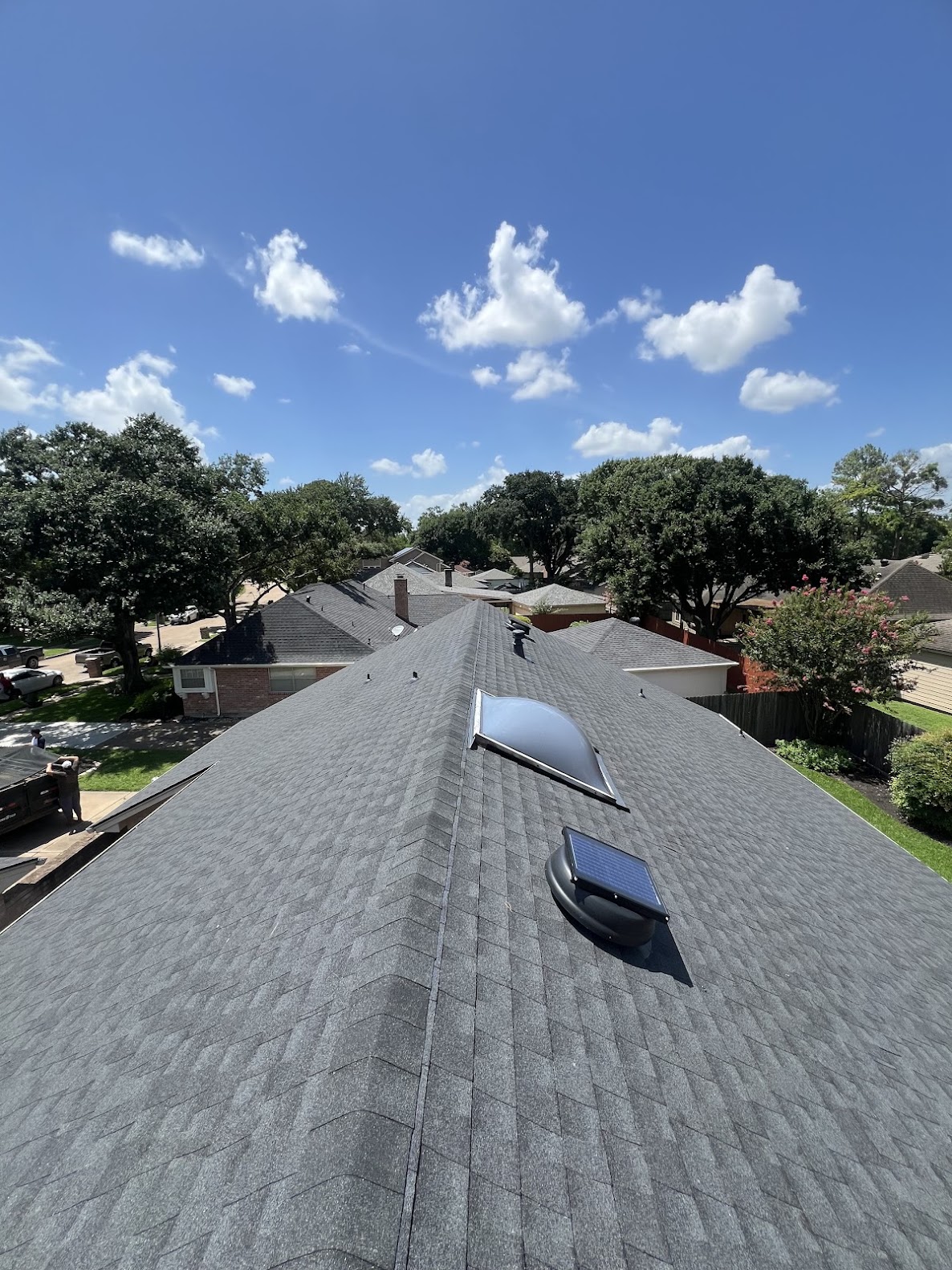 Completed residential shingle roof detail with solar attic vent under blue sky